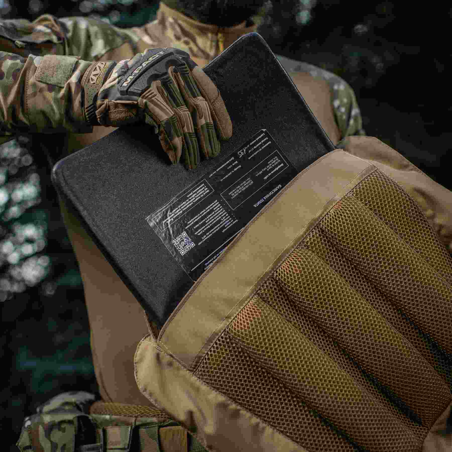 A man wearing a glove inserts a ballistic plate into a plate carrier