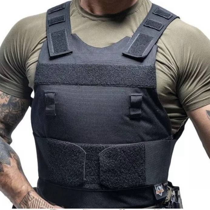 Person in a black body armor vest over a green T‑shirt