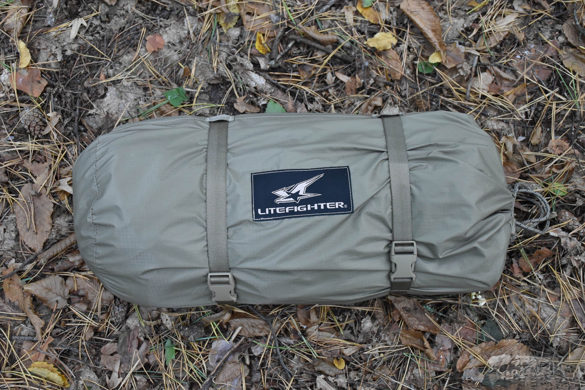 A packed tent in its bag, lying on fallen leaves