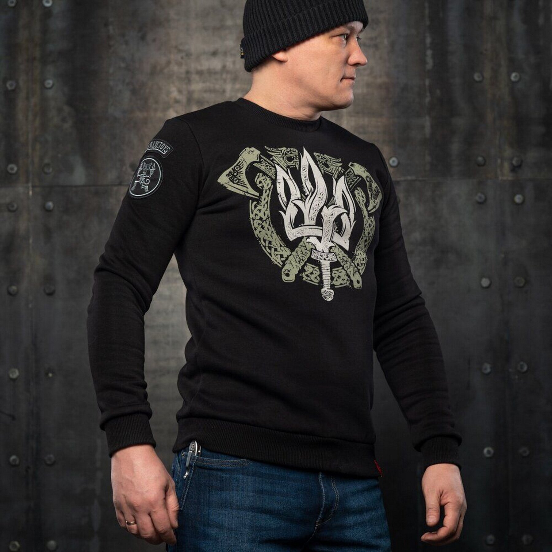 A man wearing a black sweatshirt with the Ukrainian coat of arms on the front, set against a background of crossed axes