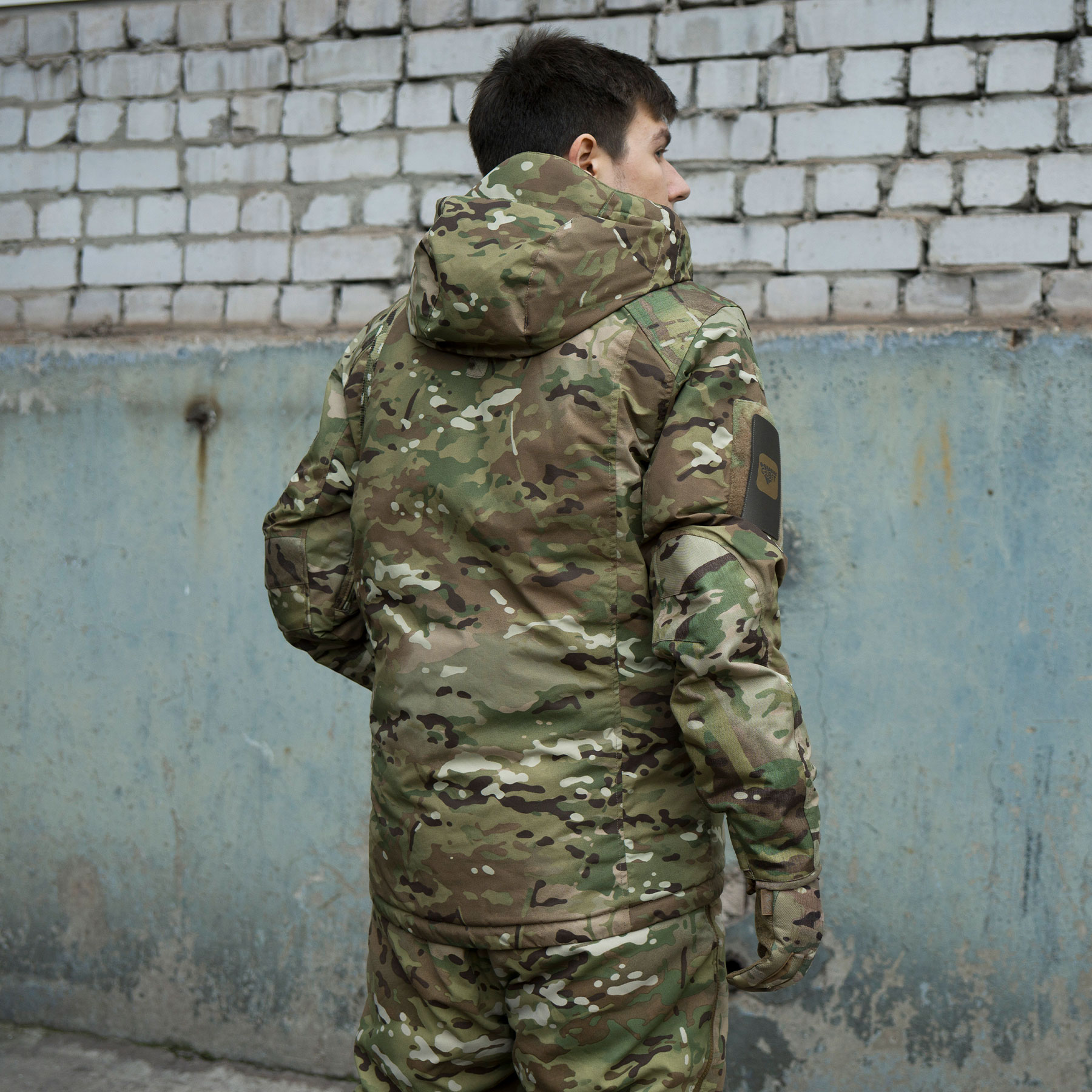 A man wearing winter tactical gear and Multicam (view from behind)