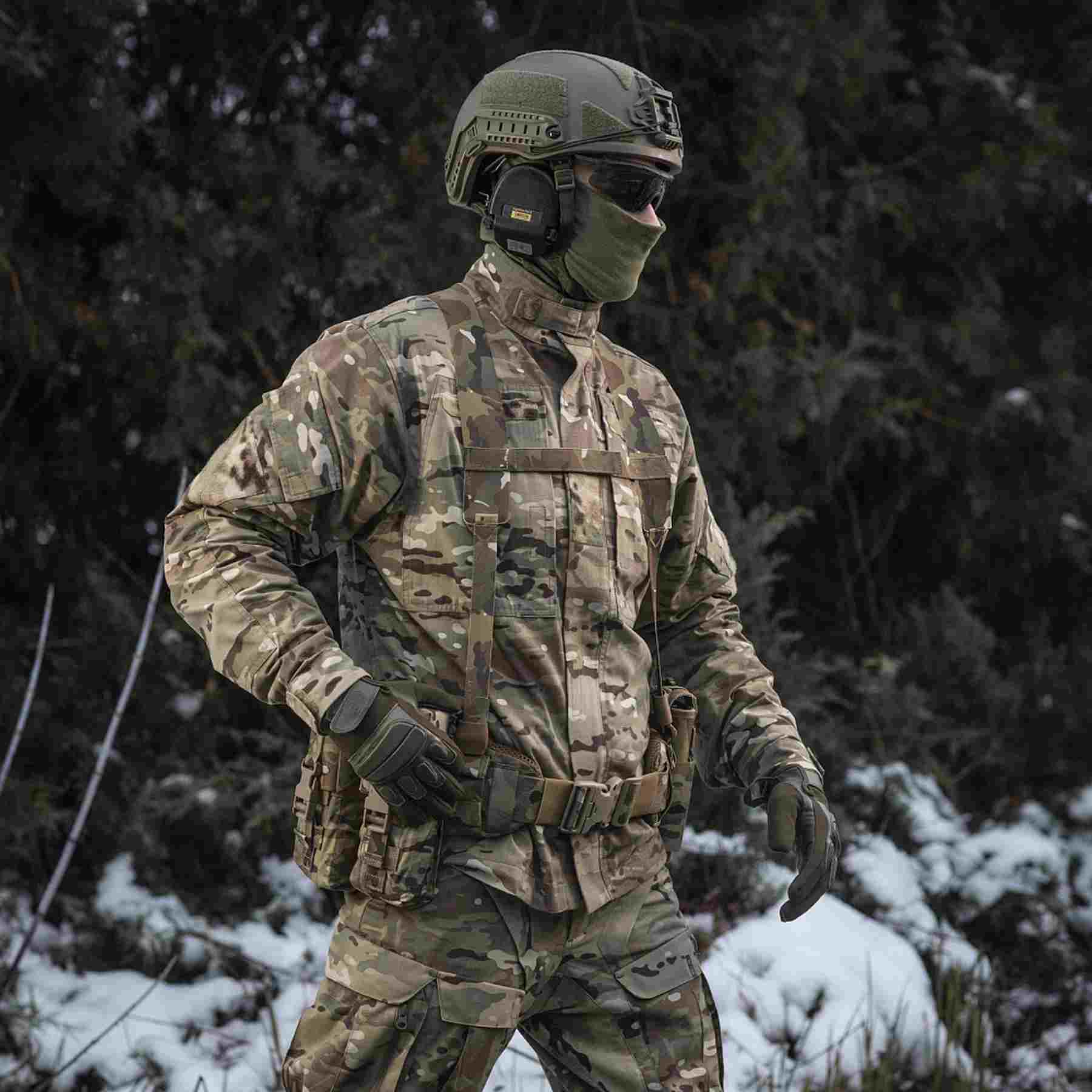 A person wearing camouflage military uniform, a helmet, and a face mask stands in a snow-covered forest